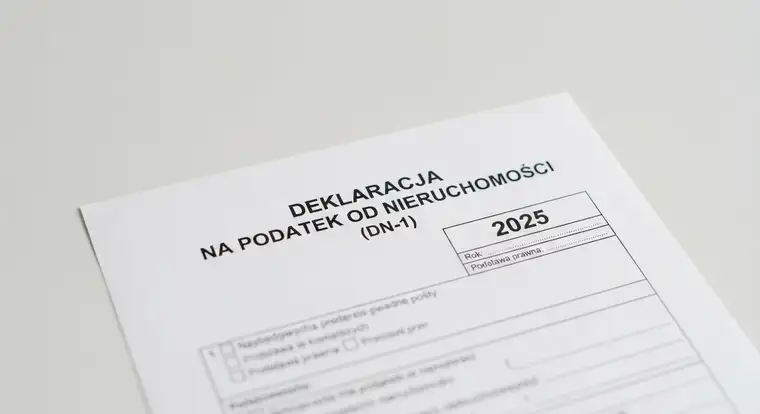 Wypełnianie formularza deklaracji na podatek od nieruchomości 2025 z dokumentami, długopisem i okularami na biurku